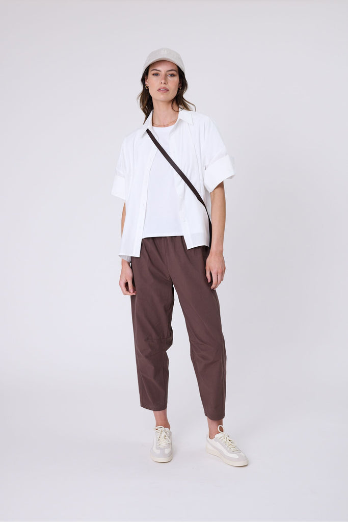 Woman wearing a white t-shirt and brown pants on a white background. Marlow white Barrel Tee.