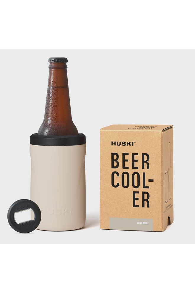 A limited edition Huski beer cooler in sand beige, with a bottle of beer inserted, sits beside its packaging box and a bottle opener on a white background.