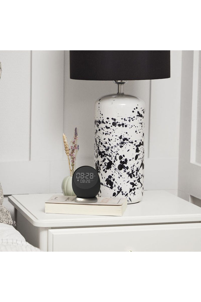 Kreafunk Black Bell Alarm Clock sitting on top of a book under a table lamp