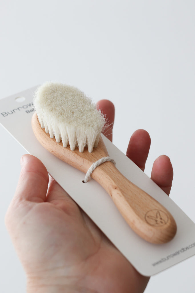 Burrow_Be_Baby_Hair_Brush. Image shows hair brush on a hang cell cardboard backing being held in a women's hand.