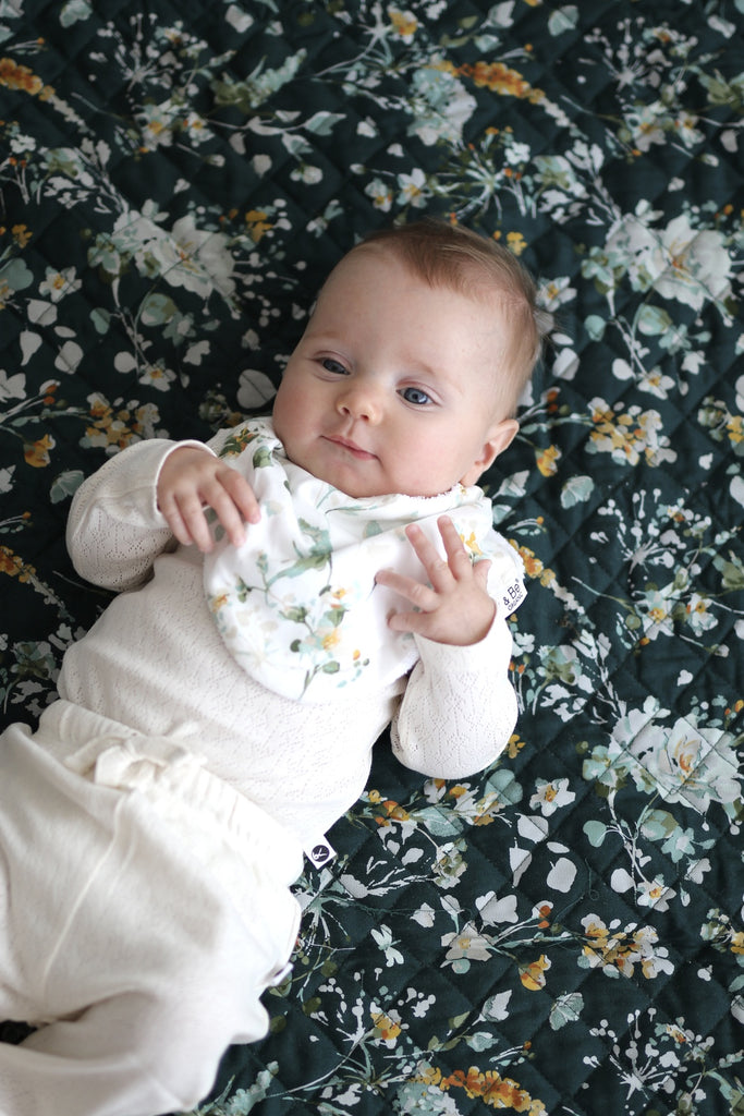 Burrow & Be Spring Melody Dribble Bib  Image shows Baby wearing Bib whilst laying on a quilted mat.