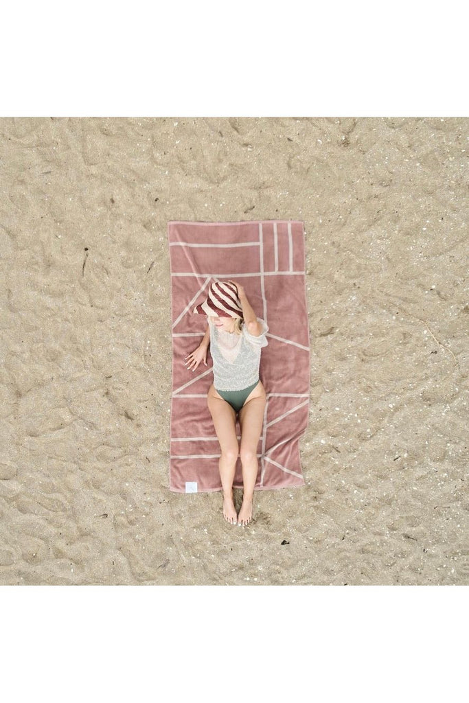 & Sunday Journey Organic Beach/Pool Towel Dune Model laying on towel. Towel is front side up showing Dune Blush with Cream Lines 