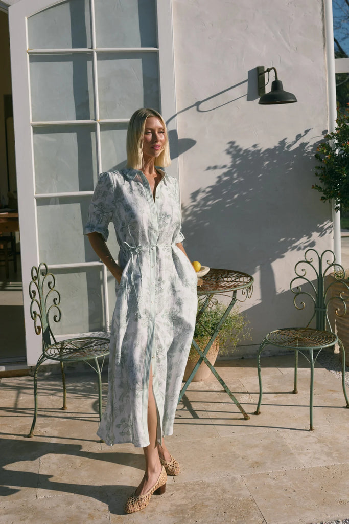 Woman wearing a light-colored dress with a subtle pattern on a plain background. Cable Melbourne Avondale Linen Dress in Palm Print.