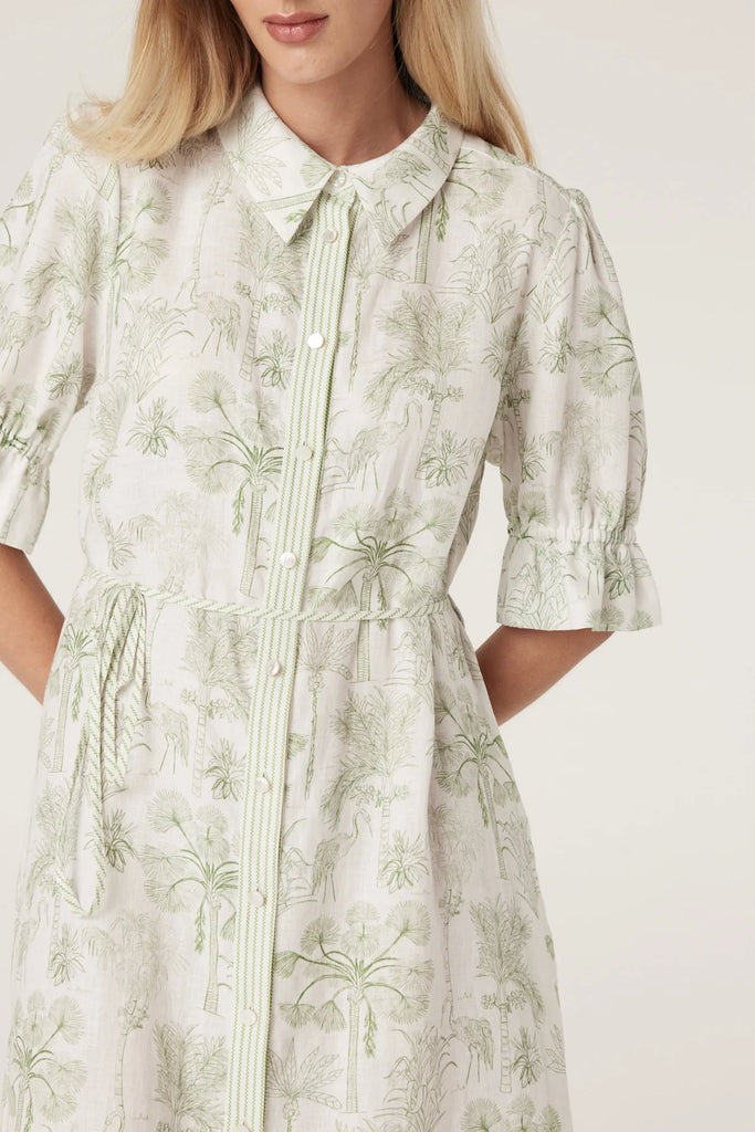 Woman wearing a light-colored dress with a subtle pattern on a plain background. Cable Melbourne Avondale Linen Dress in Palm Print.