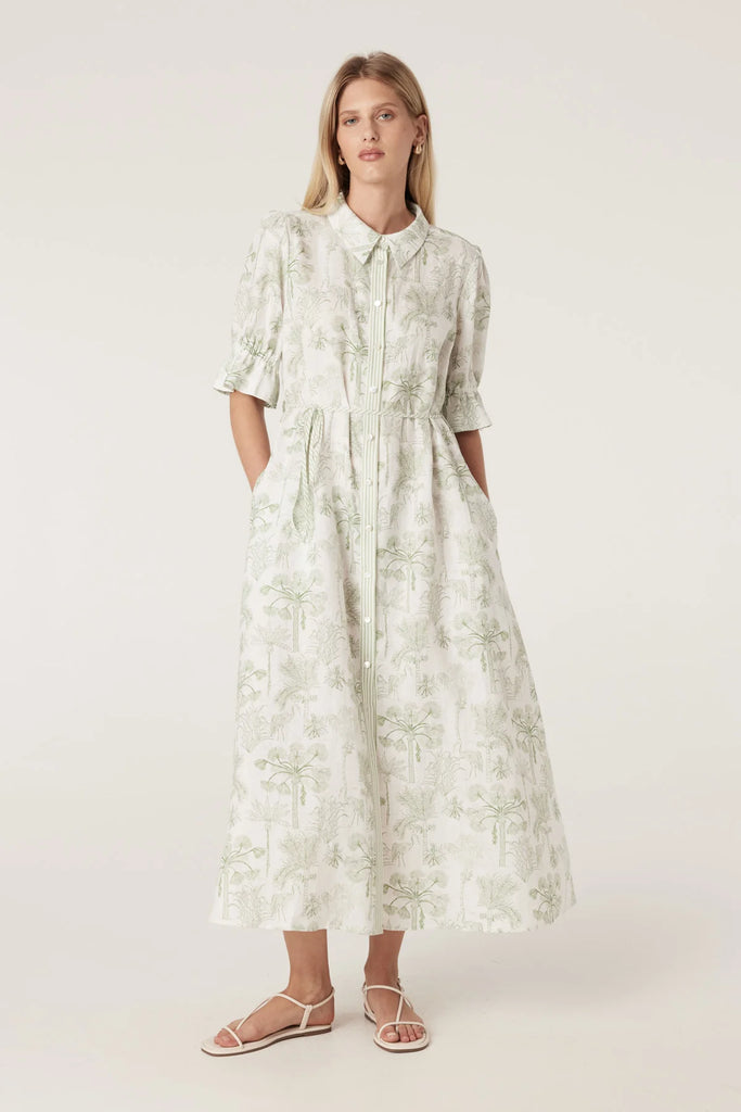 Woman wearing a light-colored dress with a subtle pattern on a plain background. Cable Melbourne Avondale Linen Dress in Palm Print.