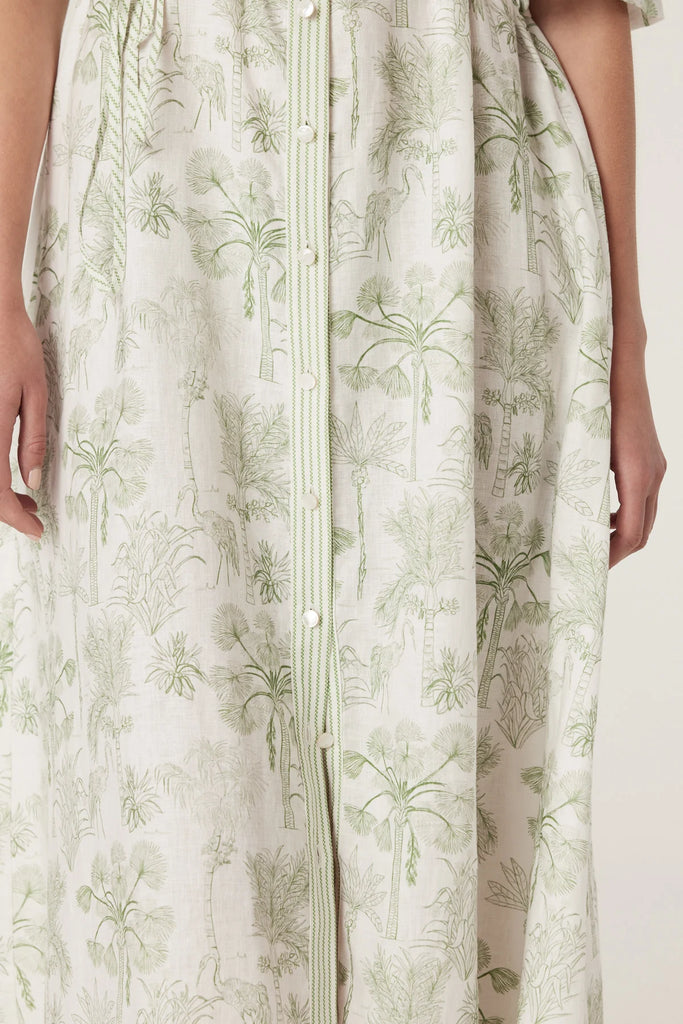 Woman wearing a light-colored dress with a subtle pattern on a plain background. Cable Melbourne Avondale Linen Dress in Palm Print.