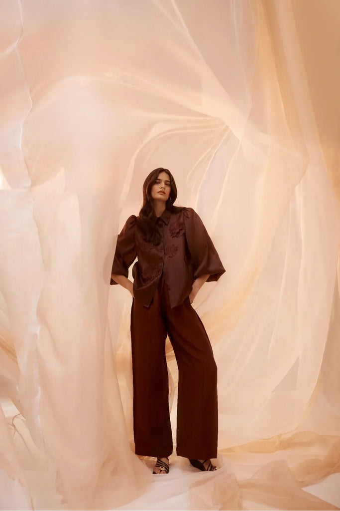 Woman wearing a brown blouse with floral embellishments and matching pants. Cable Goldie Pant and Mirage Blouse in Raisin.