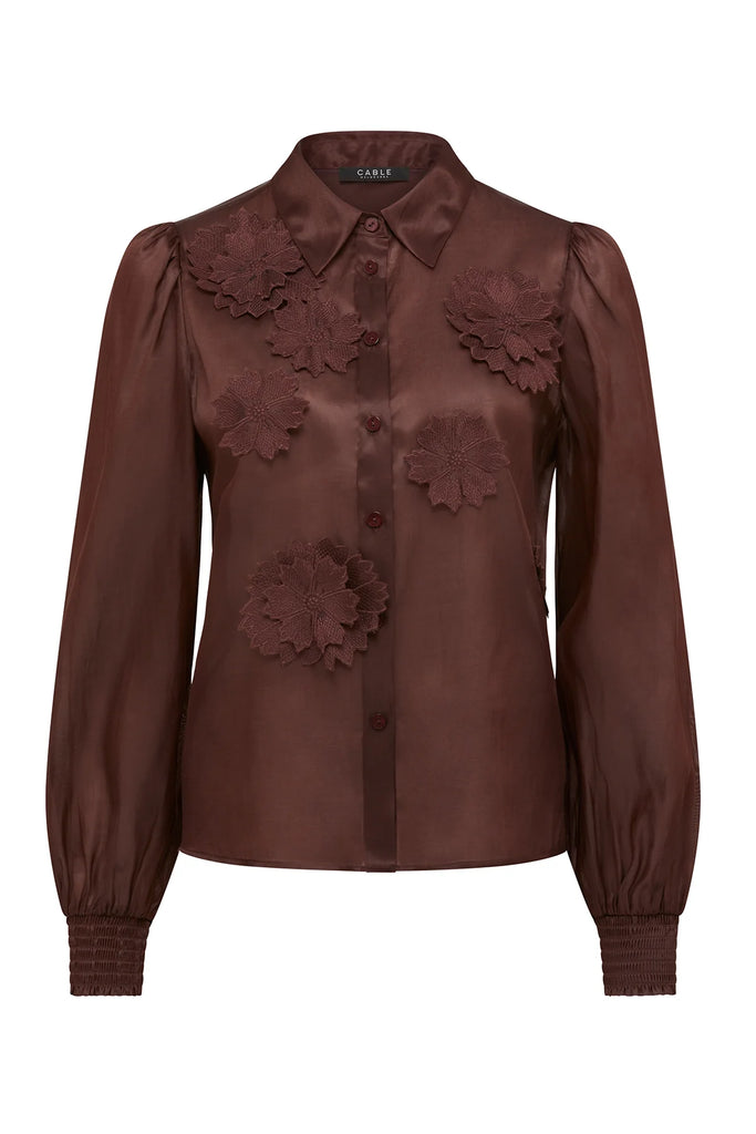 brown blouse with floral details on a plain background. Cable Mirage Blouse in raisin.