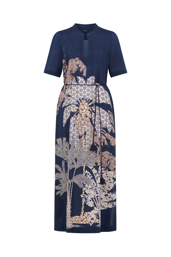 Woman wearing a navy blue top and patterned dress on a white background. Cable Pina Kaftan Dress in Mirage Print.