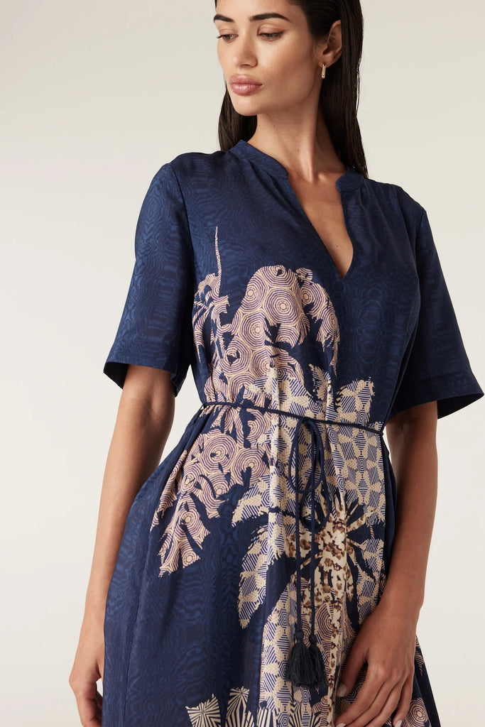 Woman wearing a navy blue top and patterned dress on a white background. Cable Pina Kaftan Dress in Mirage Print.