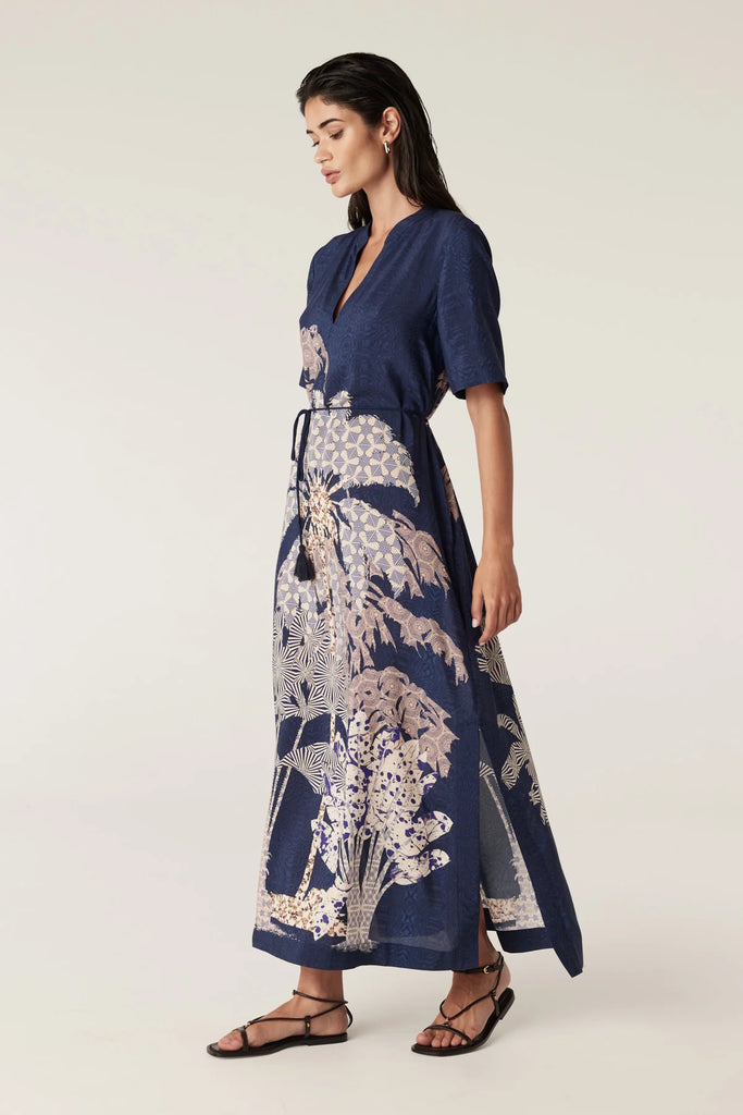 Woman wearing a navy blue top and patterned dress on a white background. Cable Pina Kaftan Dress in Mirage Print.