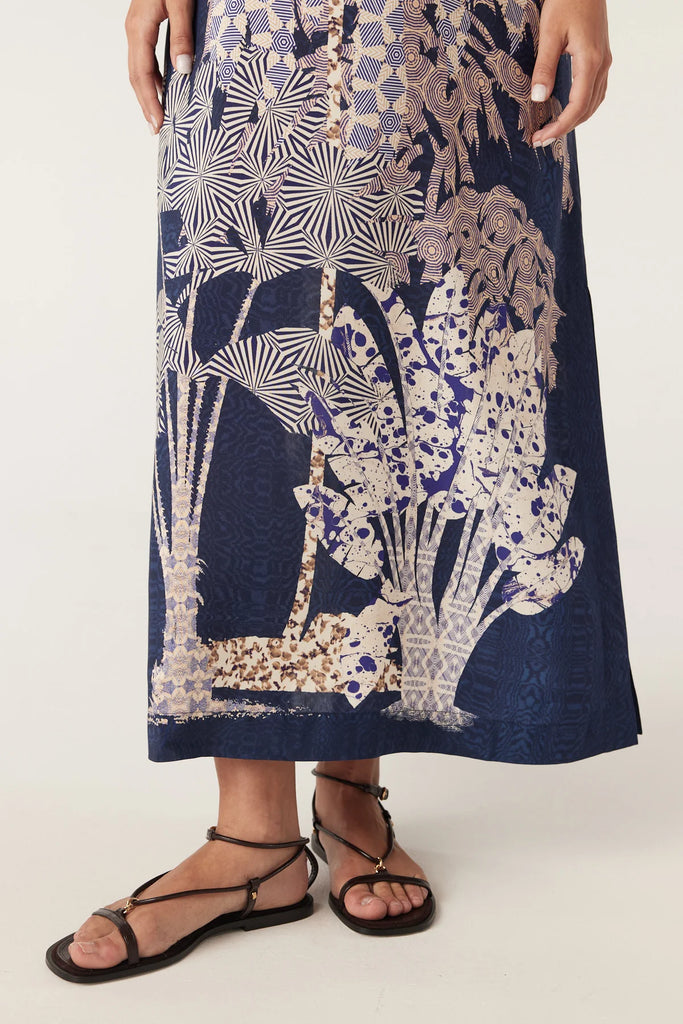 Woman wearing a navy blue top and patterned dress on a white background. Cable Pina Kaftan Dress in Mirage Print.