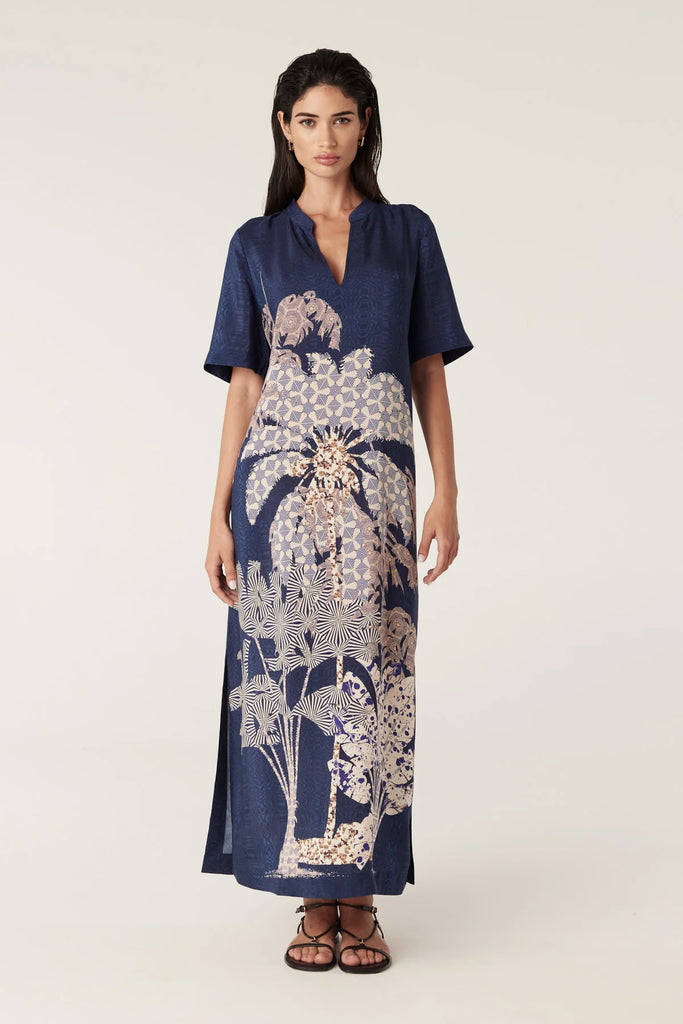 Woman wearing a navy blue top and patterned dress on a white background. Cable Pina Kaftan Dress in Mirage Print.