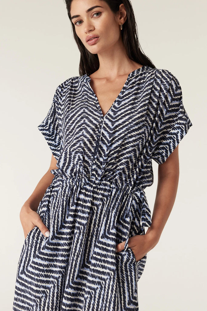 Woman wearing a blue and white patterned dress on a plain background. Cable Seabreeze dress in chevron print.