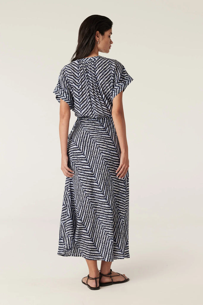 Woman wearing a blue and white patterned dress on a plain background. Cable Seabreeze dress in chevron print.