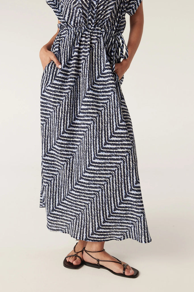 Woman wearing a blue and white patterned dress on a plain background. Cable Seabreeze dress in chevron print.