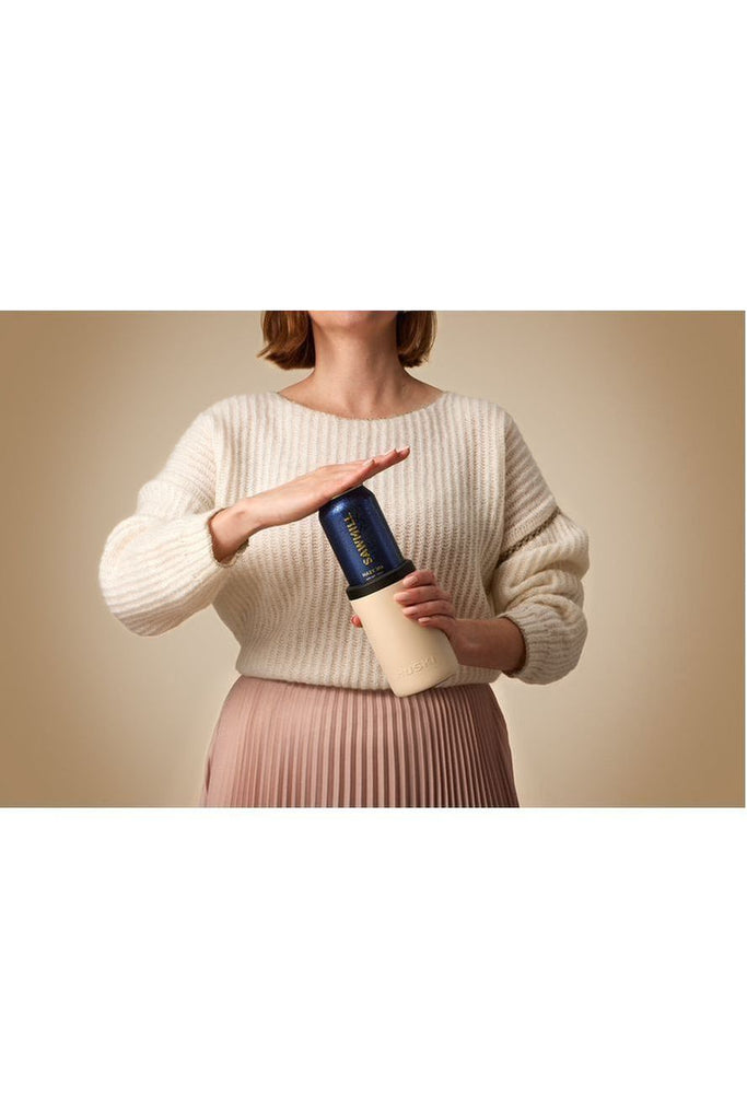 Discover the limited edition sand beige Huski Beer Cooler! A woman pops a blue beer can into the cooler, perfectly complementing the beautiful beige backdrop.