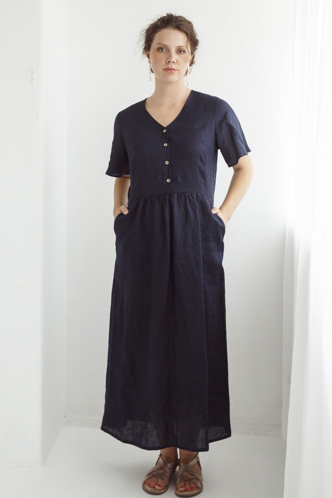 Woman wearing a navy blue dress with a plain white background. Dalston Evie Dress in Ink. 100% Linen.