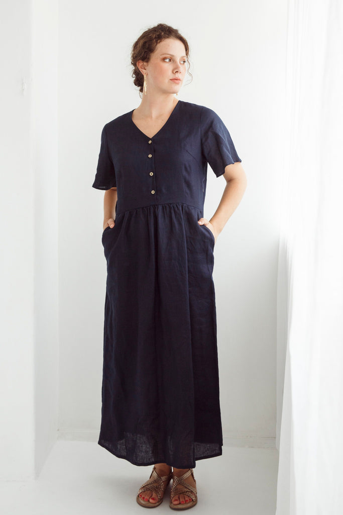 Woman wearing a navy blue dress with a plain white background. Dalston Evie Dress in Ink. 100% Linen.