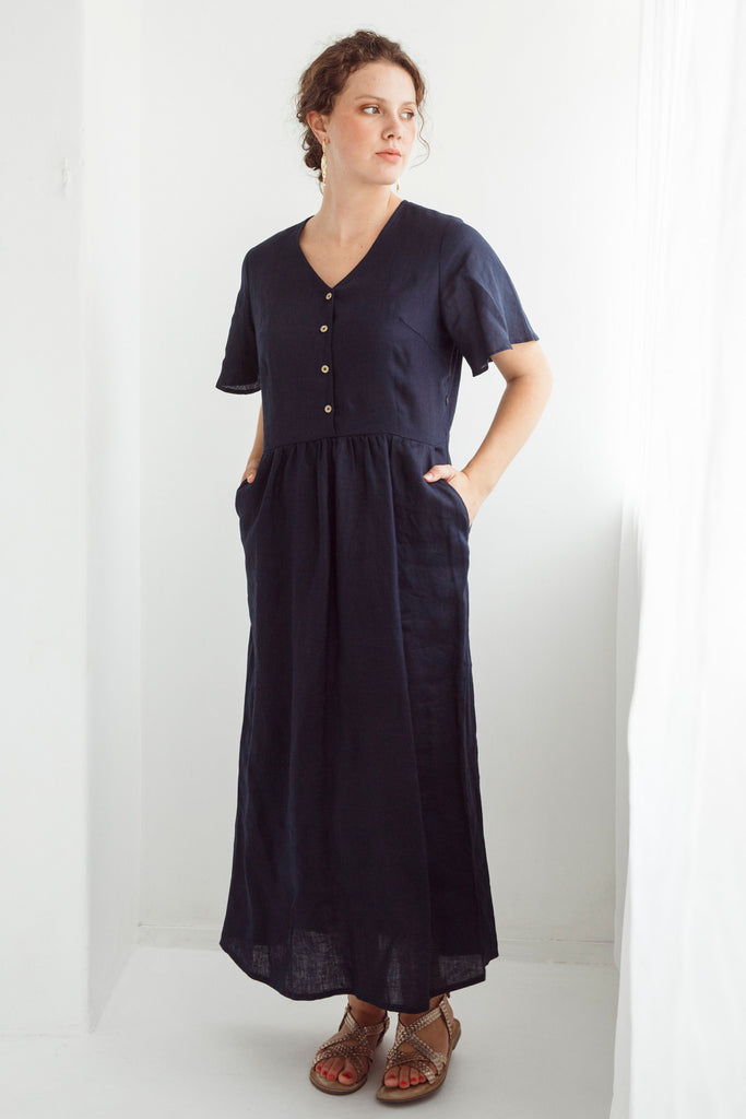 Woman wearing a navy blue dress with a plain white background. Dalston Evie Dress in Ink. 100% Linen.