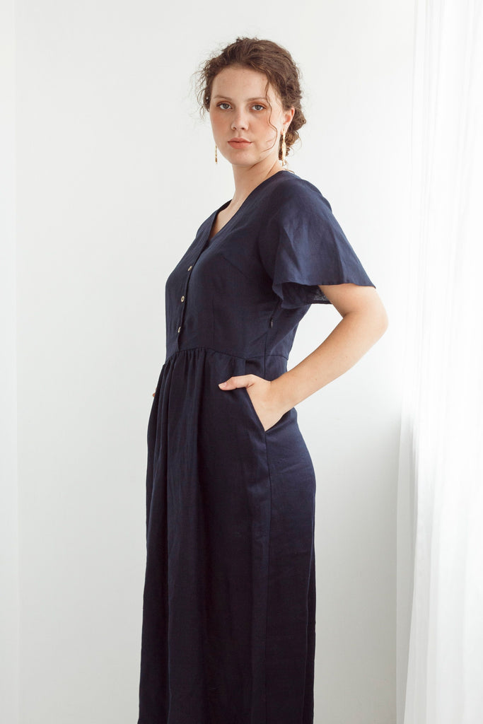 Woman wearing a navy blue dress with a plain white background. Dalston Evie Dress in Ink. 100% Linen.