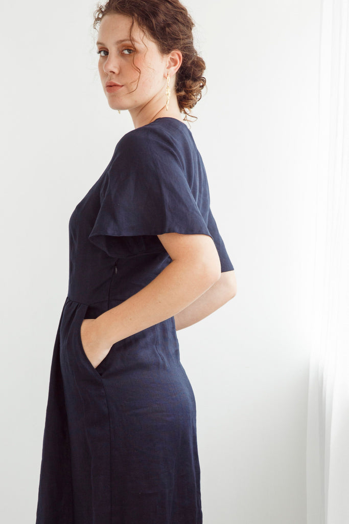 Woman wearing a navy blue dress with a plain white background. Dalston Evie Dress in Ink. 100% Linen.