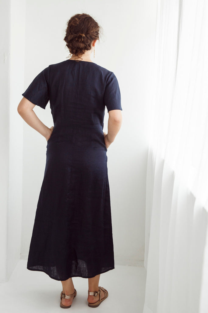 Woman wearing a navy blue dress with a plain white background. Dalston Evie Dress in Ink. 100% Linen.