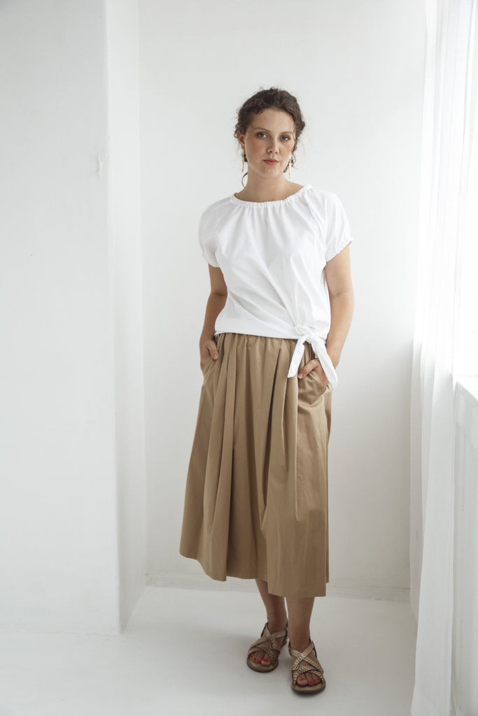 Woman wearing a white top and beige skirt against a white background. Dalston Tizzy top in white with the Sapphire Skirt in Sand.