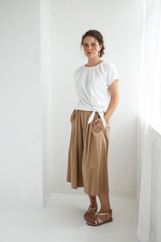 Woman wearing a white top and beige skirt against a white background. Dalston Sapphire Skirt in Sand worn with the Dalston Tizzy Top in White.
