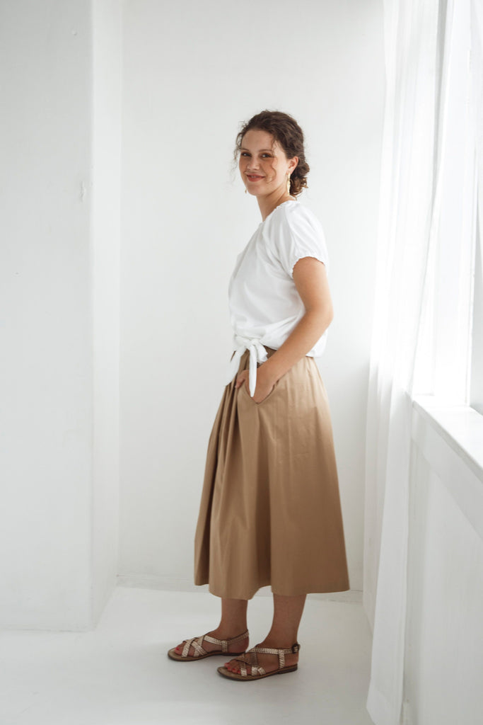 Woman wearing a white top and beige skirt against a white background. Dalston Sapphire Skirt in Sand worn with the Dalston Tizzy Top in White.