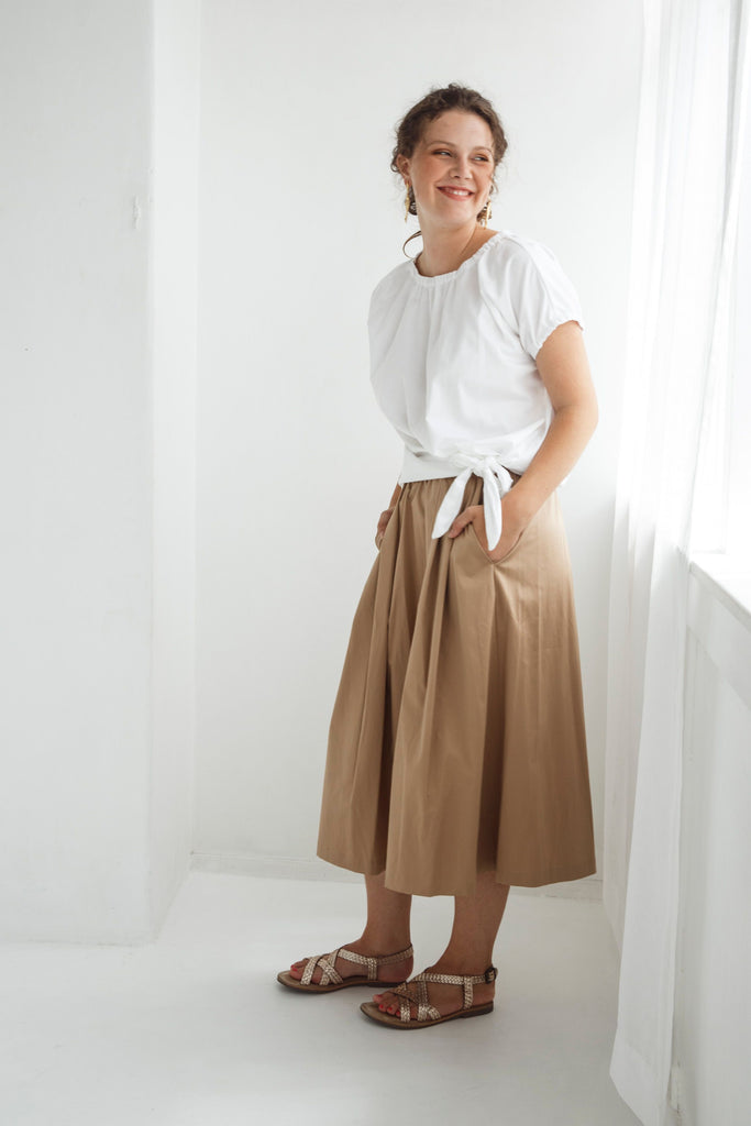 Woman wearing a white top and beige skirt against a white background. Dalston Sapphire Skirt in Sand worn with the Dalston Tizzy Top in White.