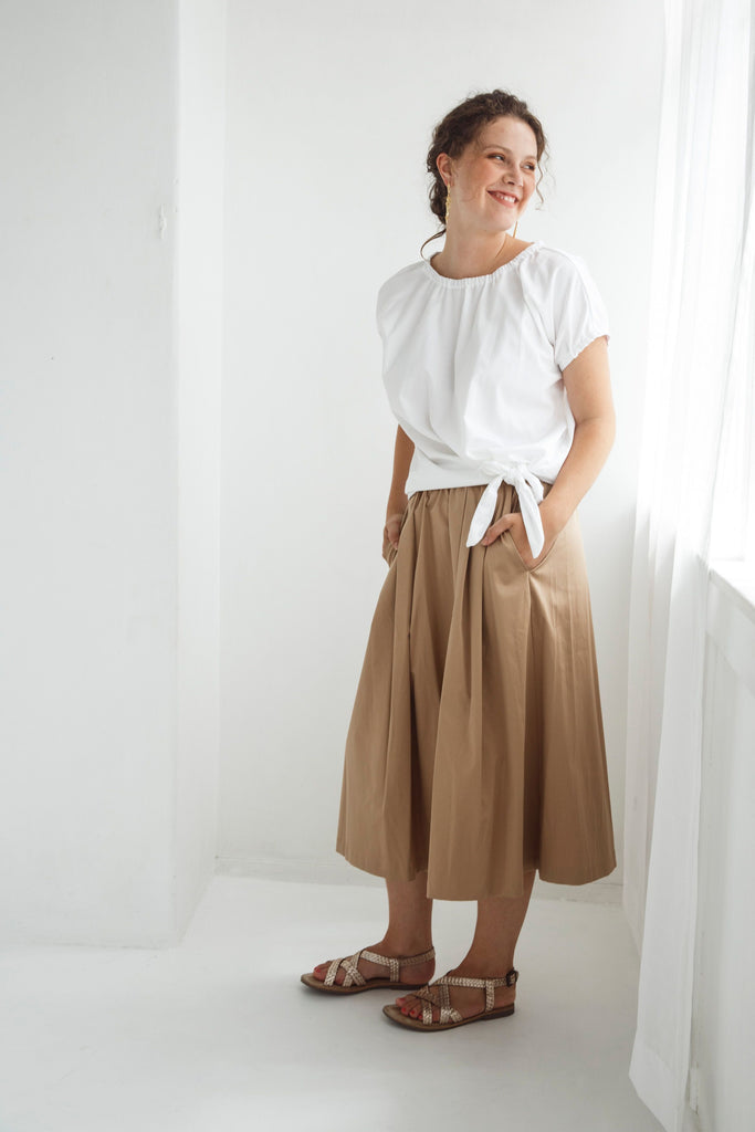 Woman wearing a white top and beige skirt against a white background. Dalston Tizzy top in white with the Sapphire Skirt in Sand.
