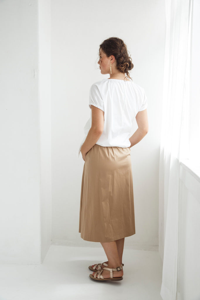 Woman wearing a white top and beige skirt against a white background. Dalston Sapphire Skirt in Sand worn with the Dalston Tizzy Top in White.
