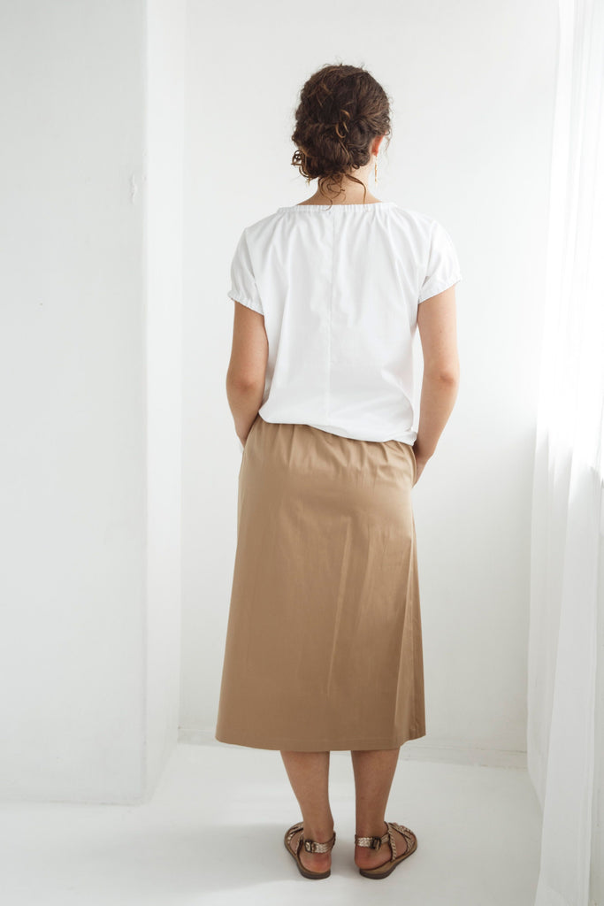 Woman wearing a white top and beige skirt against a white background. Dalston Tizzy top in white with the Sapphire Skirt in Sand.