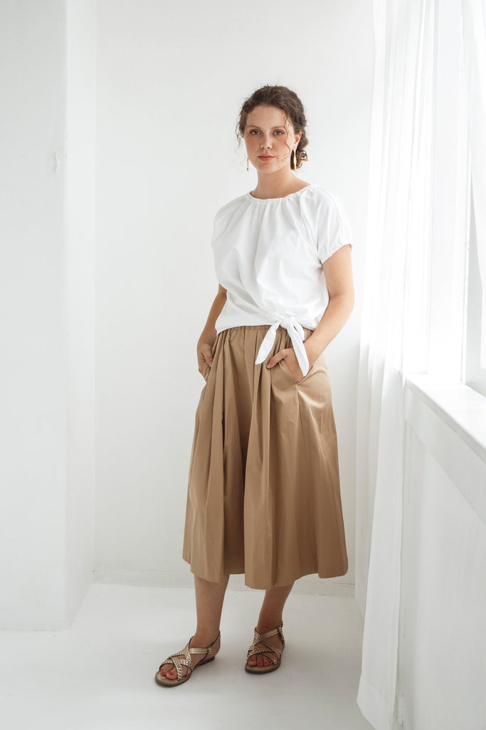 Woman wearing a white top and beige skirt against a white background. Dalston Sapphire Skirt in Sand worn with the Dalston Tizzy Top in White.