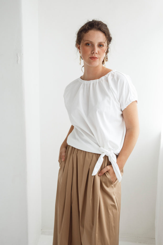 Woman wearing a white top and beige skirt against a white background. Dalston Tizzy top in white with the Sapphire Skirt in Sand.