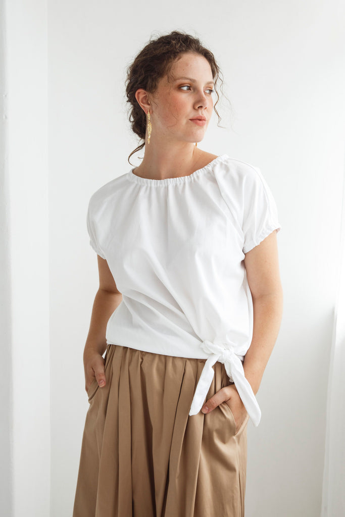Woman wearing a white top and beige skirt against a white background. Dalston Tizzy top in white with the Sapphire Skirt in Sand.