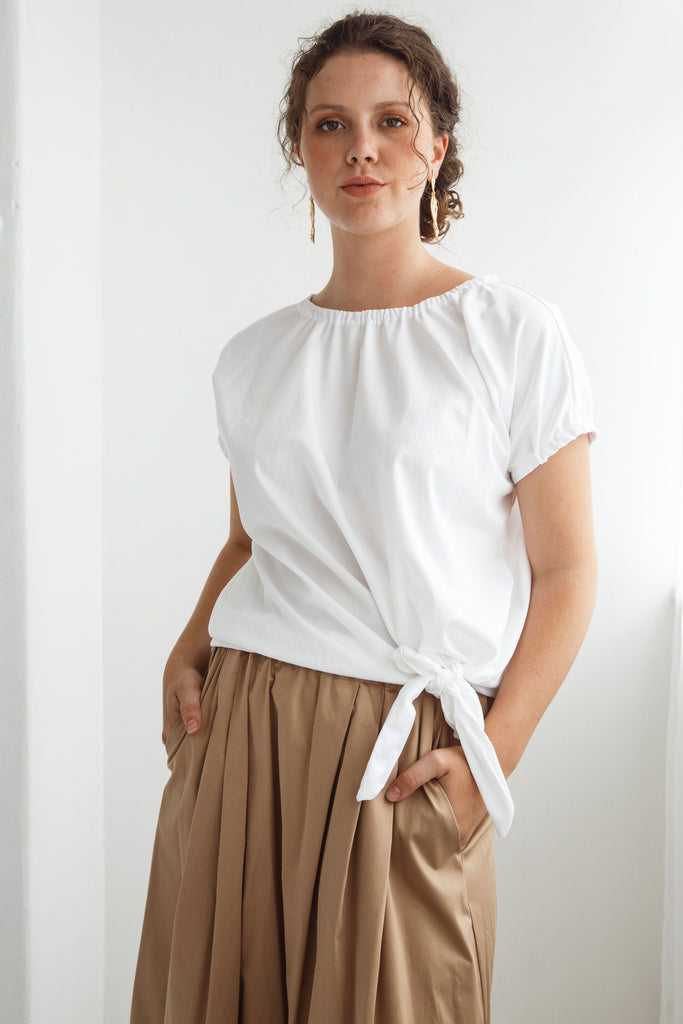 Woman wearing a white top and beige skirt against a white background. Dalston Tizzy top in white with the Sapphire Skirt in Sand.
