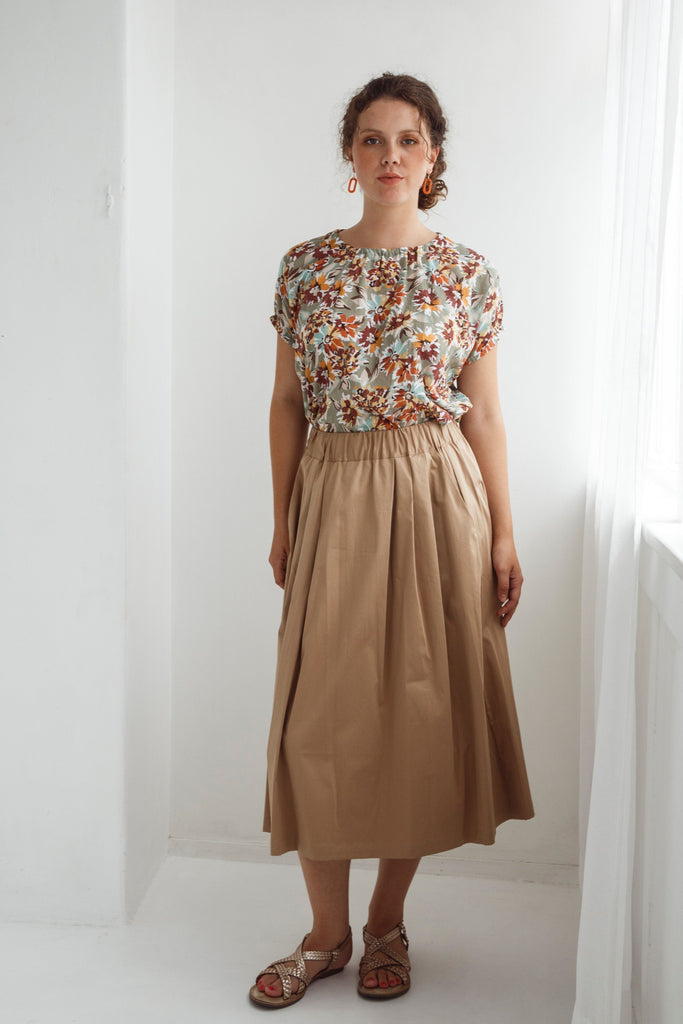 Woman wearing a floral top and beige skirt against a white background. Dalston Sapphire Skirt in Sand