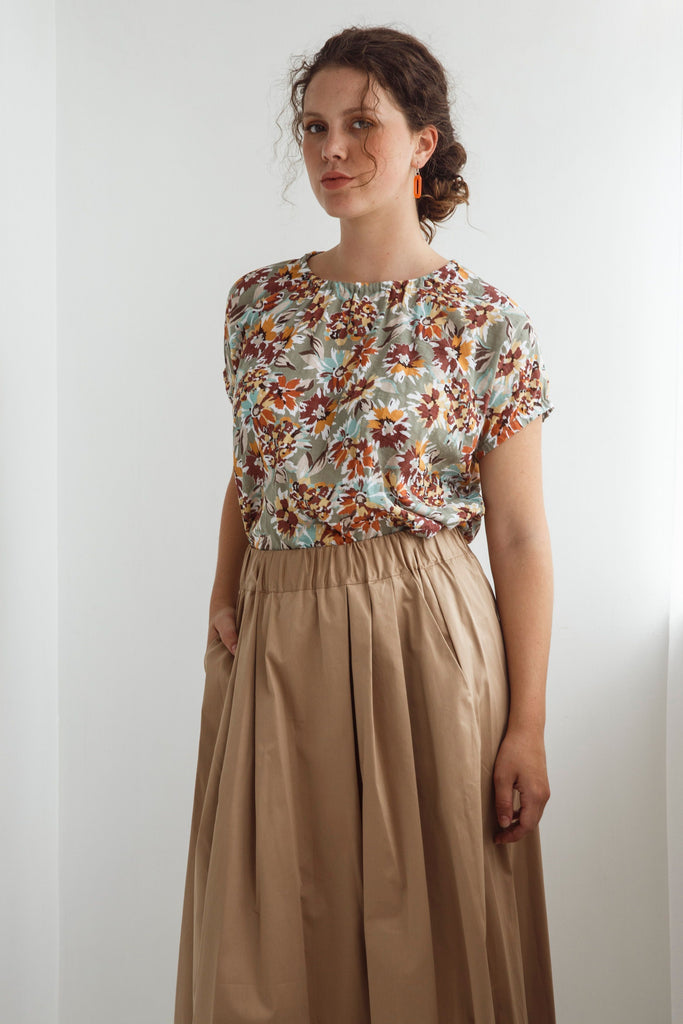 Woman wearing a floral top and beige skirt against a white background. Dalston Sapphire Skirt in Sand