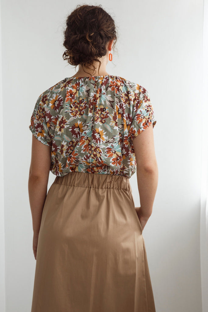 Woman wearing a floral top and beige skirt against a white background. Dalston Sapphire Skirt in Sand