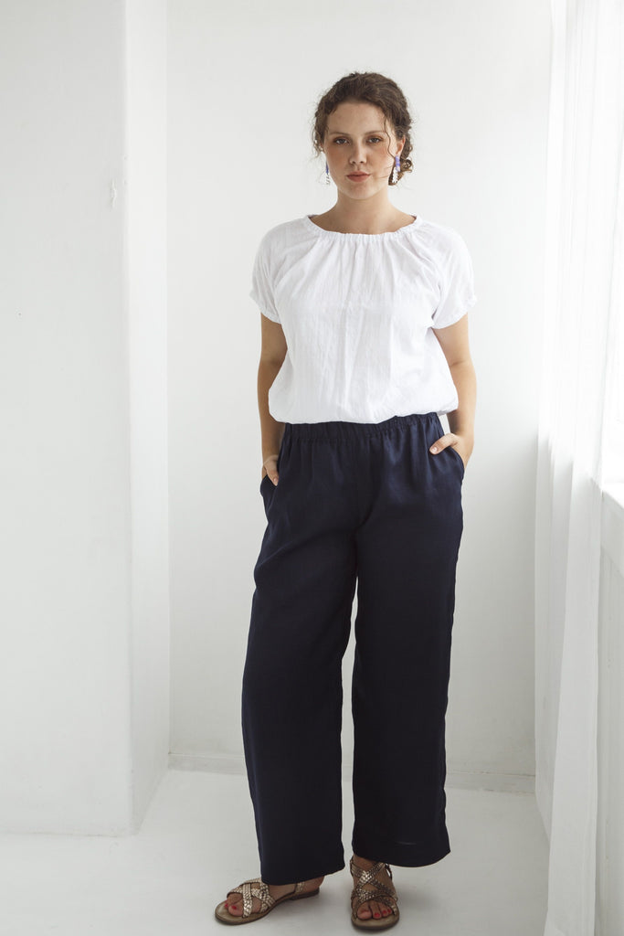 Woman wearing a white blouse and dark pants against a white background. Dalston Ruby Pant in Ink.