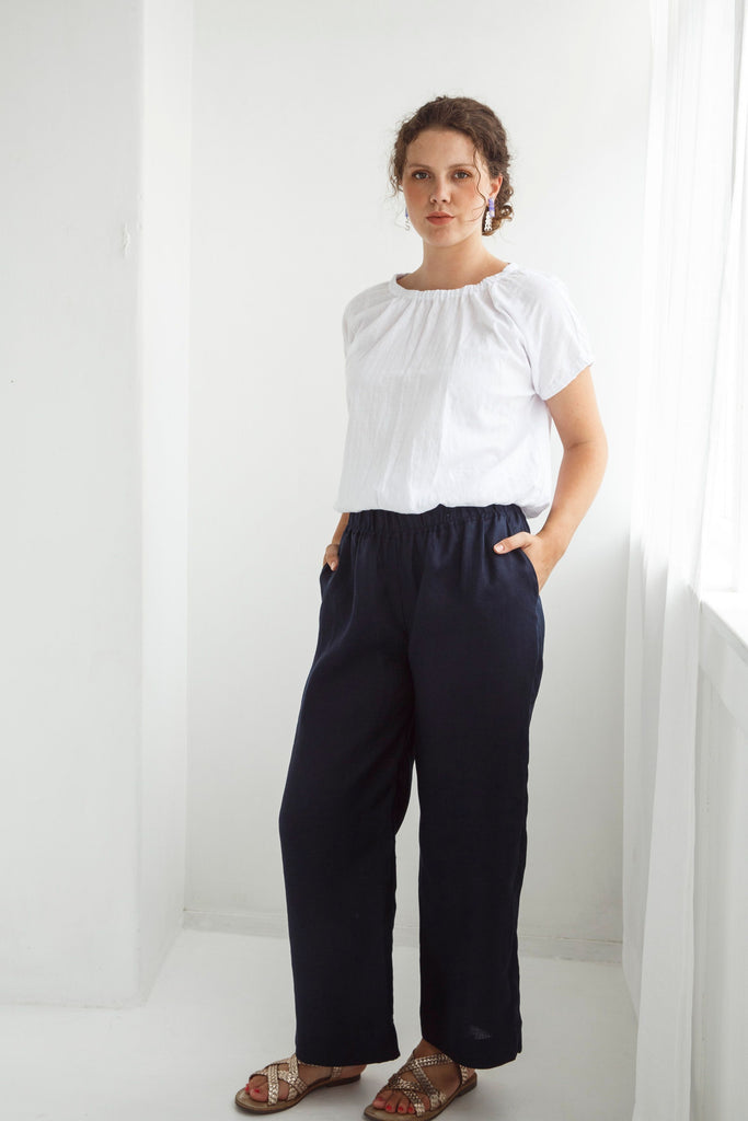 Woman wearing a white blouse and dark pants against a white background. Dalston Ruby Pant in Ink.