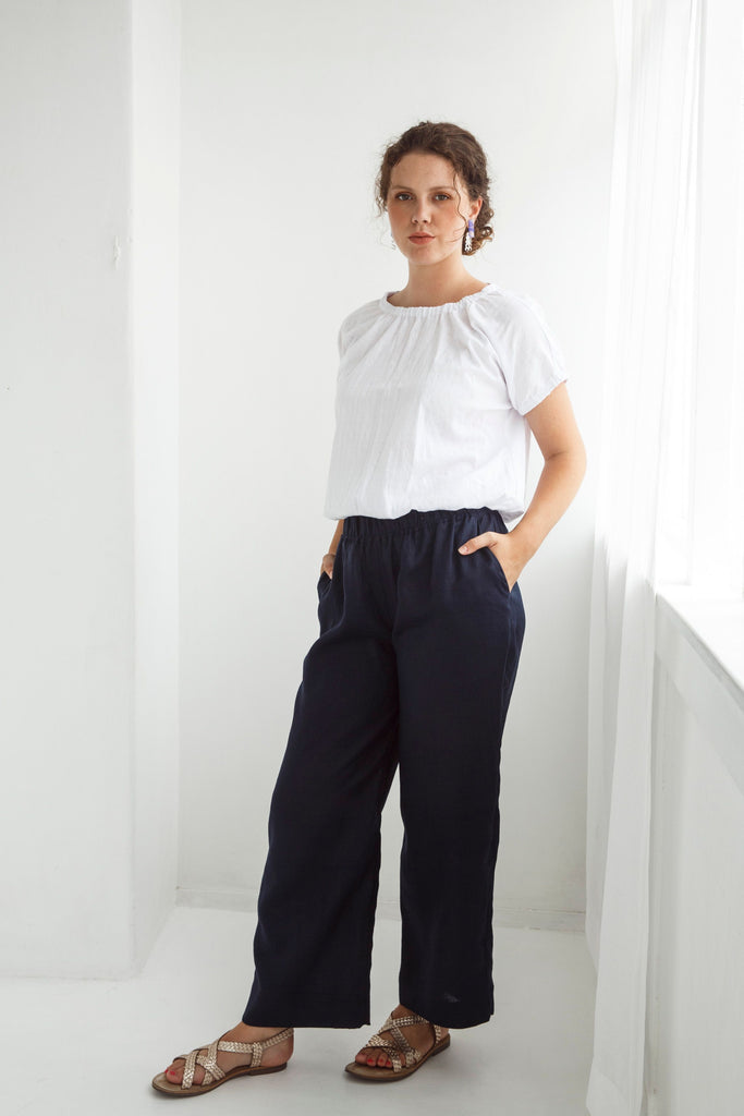 Woman wearing a white blouse and dark pants against a white background. Dalston Ruby Pant in Ink.