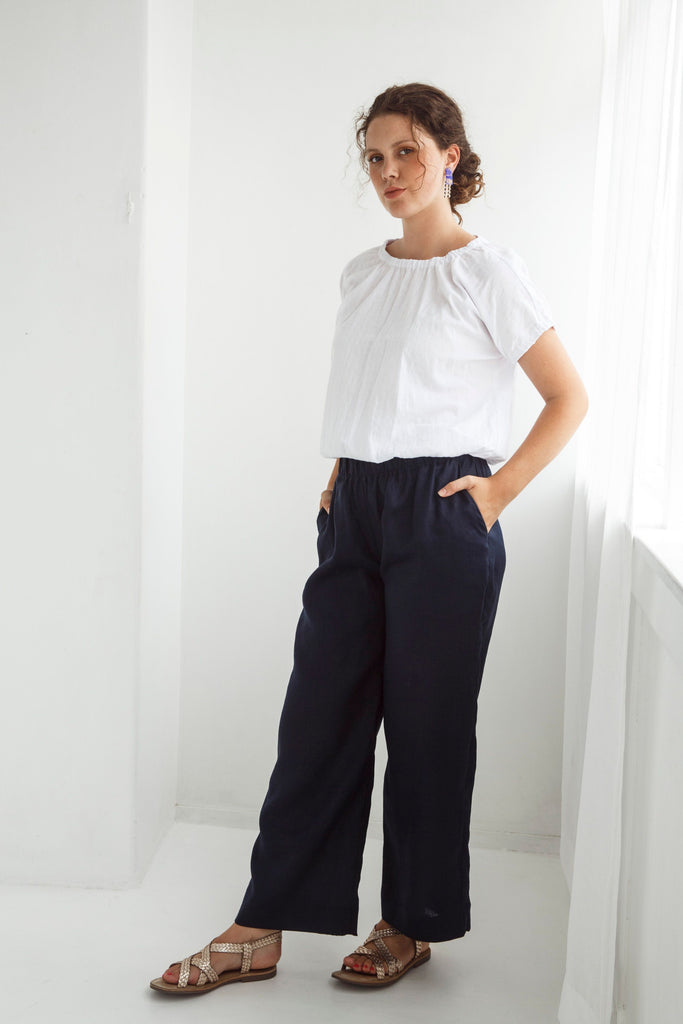 Woman wearing a white blouse and dark pants against a white background. Dalston Ruby Pant in Ink.