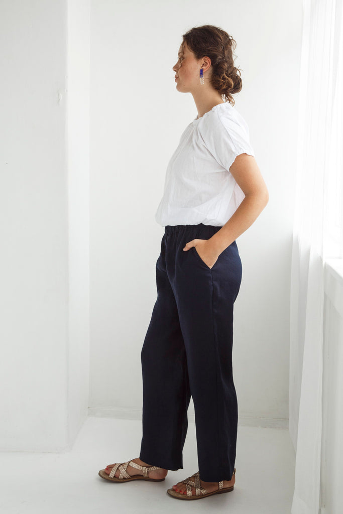 Woman wearing a white blouse and dark pants against a white background. Dalston Ruby Pant in Ink.