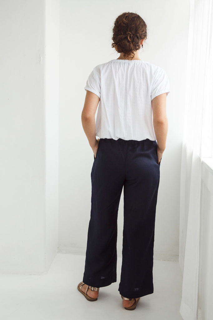 Woman wearing a white blouse and dark pants against a white background. Dalston Ruby Pant in Ink.