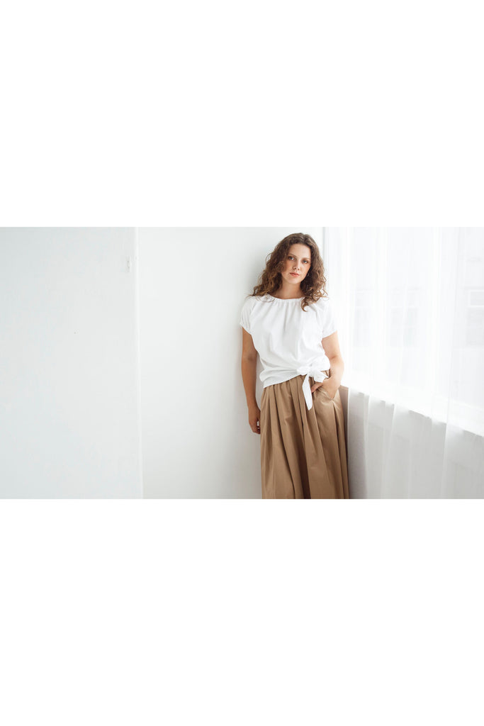 Woman wearing a white top and beige skirt against a white background. Dalston Tizzy top in white with the Sapphire Skirt in Sand.