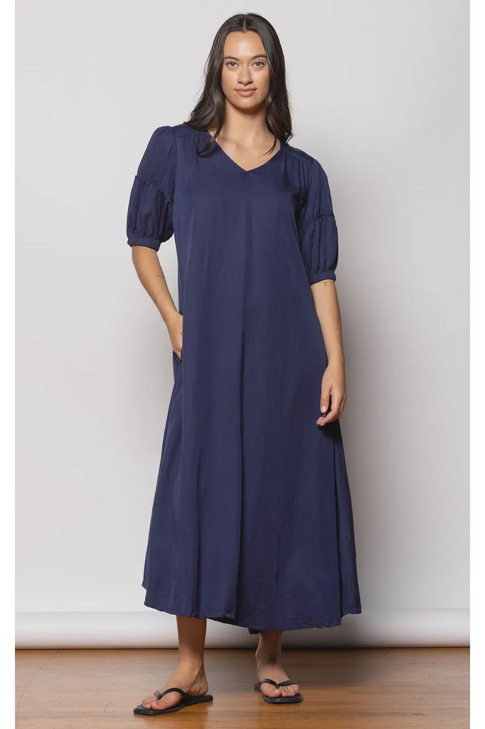 Woman wearing a navy blue dress with puff sleeves against a white background. Dressed Trestle Dress in Navy