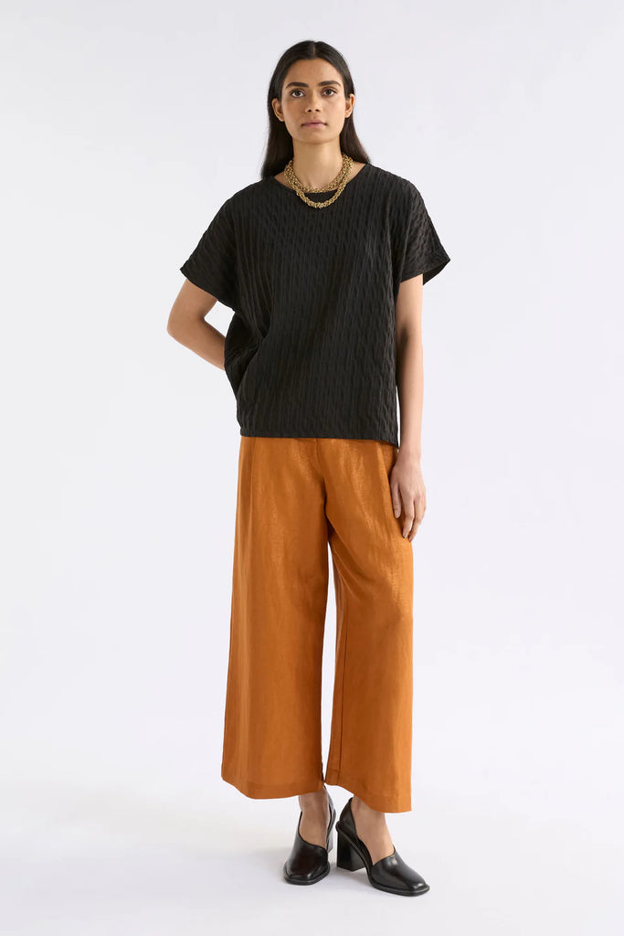 Woman wearing an Elk black textured top and orange pants on a white background